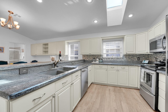 kitchen featuring sink, light hardwood / wood-style flooring, appliances with stainless steel finishes, lofted ceiling with skylight, and an inviting chandelier