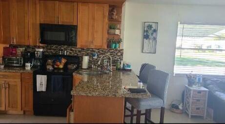 kitchen featuring light stone countertops, sink, tasteful backsplash, a kitchen bar, and black appliances