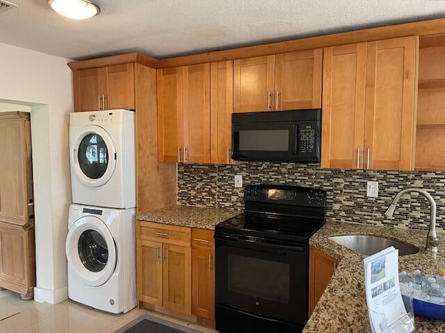 kitchen featuring stone counters, sink, stacked washing maching and dryer, decorative backsplash, and black appliances