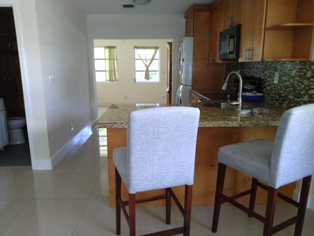 814 W Ocean Dr, Boynton Beach, FL 33426 - kitchen with black microwave, freestanding refrigerator, brown cabinets, electric range, and tasteful backsplash