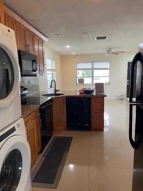 kitchen with a wealth of natural light, sink, black appliances, and stacked washer / drying machine