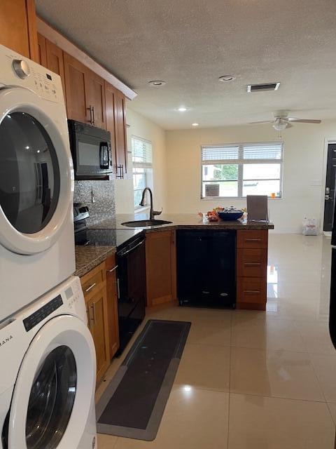 kitchen with sink, stacked washing maching and dryer, a healthy amount of sunlight, and black appliances