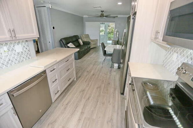 kitchen with ceiling fan, appliances with stainless steel finishes, crown molding, light hardwood / wood-style floors, and decorative backsplash