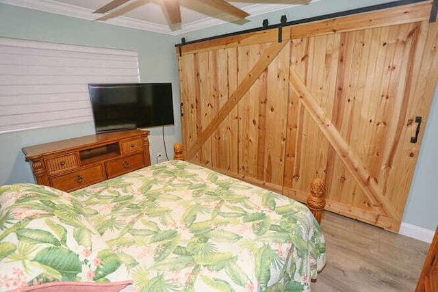 bedroom featuring ceiling fan, light hardwood / wood-style floors, crown molding, and a barn door