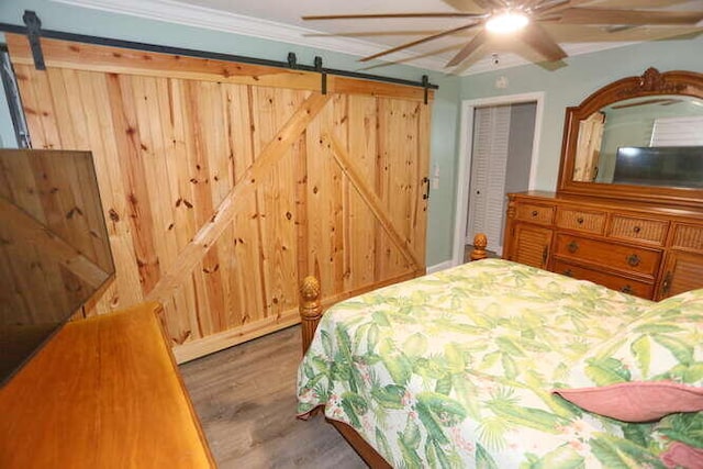 bedroom featuring a barn door, ceiling fan, dark wood-type flooring, and a closet