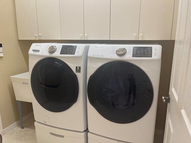 clothes washing area with cabinets, washer and dryer, and light tile patterned flooring