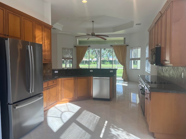 kitchen featuring black appliances, a tray ceiling, dark stone counters, and backsplash