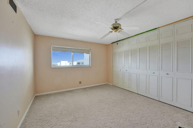 unfurnished bedroom with ceiling fan, light colored carpet, and a textured ceiling