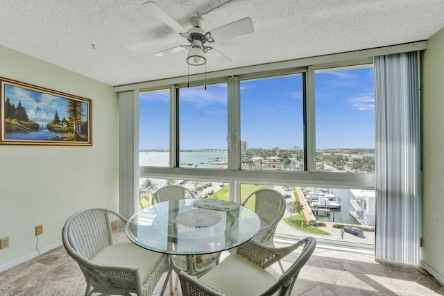 dining area featuring a textured ceiling, a water view, ceiling fan, and expansive windows