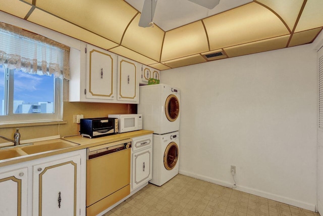 kitchen with dishwasher, stacked washer / drying machine, sink, white cabinetry, and ceiling fan