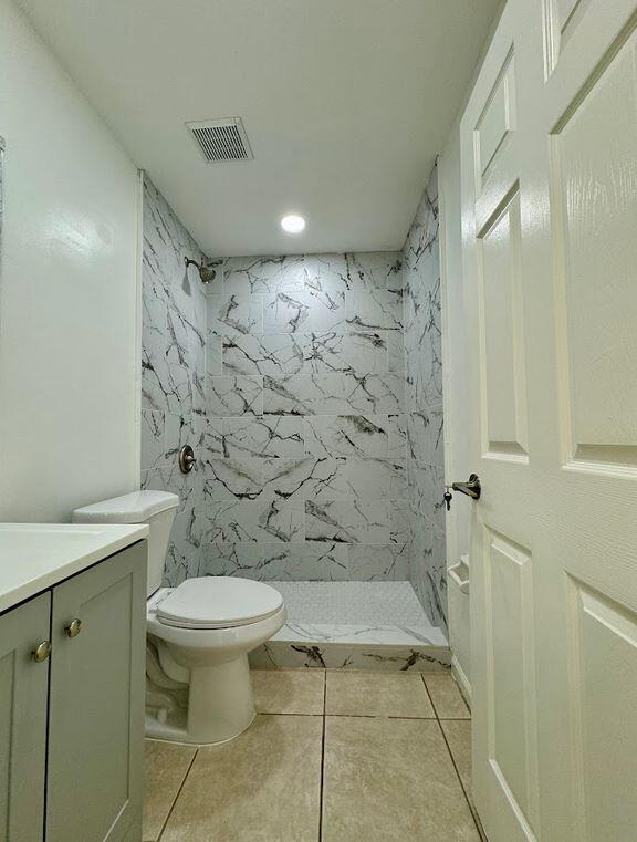 bathroom with vanity, tile patterned flooring, toilet, and tiled shower