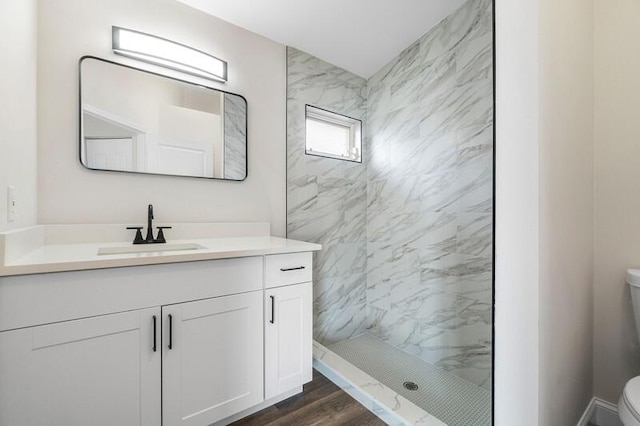 bathroom with vanity, toilet, wood-type flooring, and tiled shower