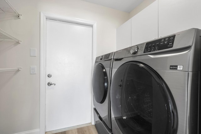 laundry room with cabinets, washing machine and dryer, and light wood-type flooring