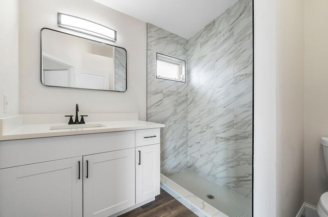 bathroom featuring tiled shower, vanity, hardwood / wood-style flooring, and toilet