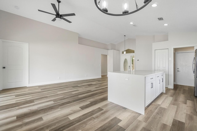 kitchen featuring white cabinetry, light hardwood / wood-style flooring, pendant lighting, a kitchen island, and ceiling fan with notable chandelier