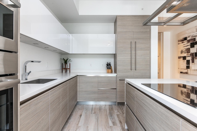 kitchen with black electric cooktop, light wood-type flooring, sink, and white cabinets