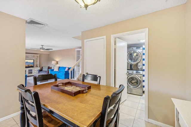 tiled dining space featuring ceiling fan, a textured ceiling, and stacked washing maching and dryer