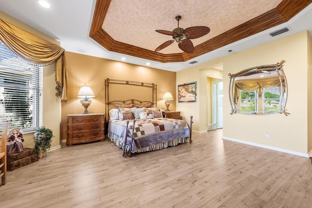 bedroom with ceiling fan, multiple windows, a tray ceiling, and light hardwood / wood-style flooring