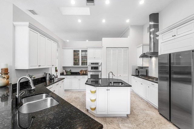 kitchen with sink, white cabinetry, wall chimney range hood, appliances with stainless steel finishes, and dark stone countertops