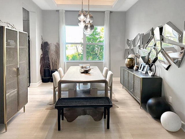 dining space with an inviting chandelier, a tray ceiling, and light hardwood / wood-style flooring