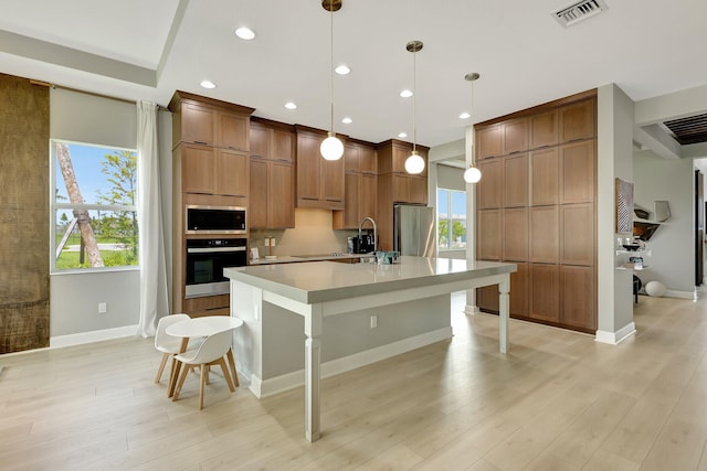 kitchen featuring a center island with sink, appliances with stainless steel finishes, hanging light fixtures, and light hardwood / wood-style floors