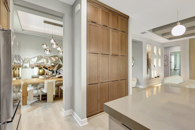 kitchen with pendant lighting, light hardwood / wood-style flooring, stainless steel fridge, and a raised ceiling