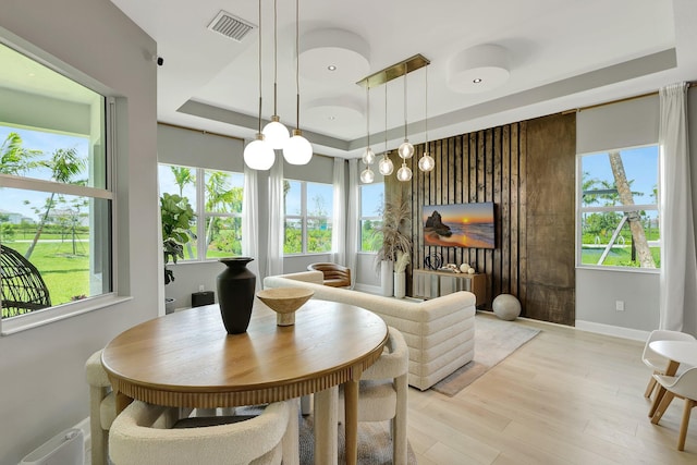 dining space featuring a raised ceiling, light wood-type flooring, plenty of natural light, and a chandelier