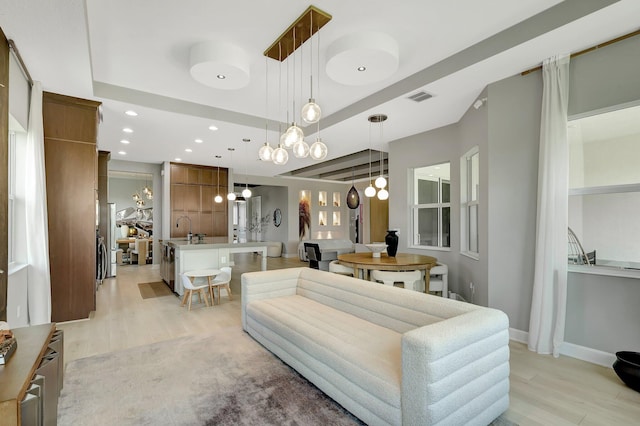 living room with a notable chandelier, light wood-type flooring, and a tray ceiling