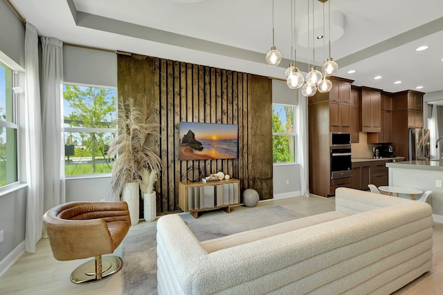 living room featuring an inviting chandelier, light wood-type flooring, a fireplace, and a tray ceiling