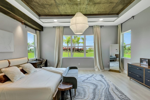 bedroom featuring light wood-type flooring, a raised ceiling, and multiple windows