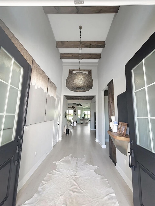 hall with light hardwood / wood-style flooring, a towering ceiling, beam ceiling, and a chandelier