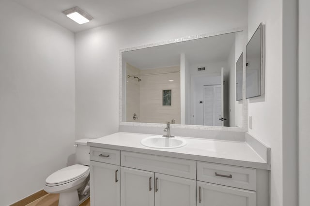 bathroom featuring a tile shower, vanity, and toilet