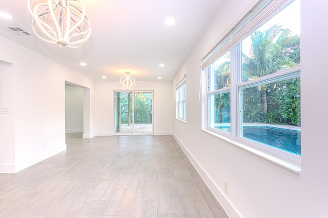 unfurnished room featuring a notable chandelier and light wood-type flooring