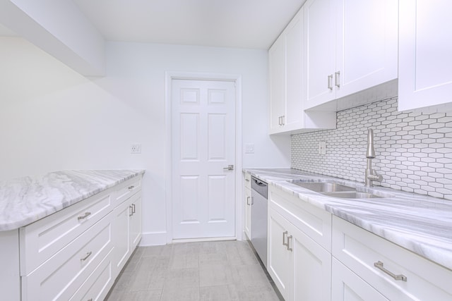 kitchen featuring light stone counters, tasteful backsplash, white cabinets, stainless steel dishwasher, and sink