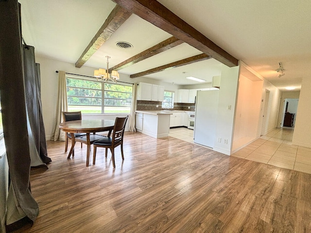 dining space featuring light hardwood / wood-style flooring, a chandelier, beamed ceiling, and sink