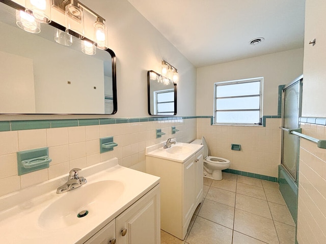 full bathroom with vanity, bath / shower combo with glass door, tile patterned floors, tile walls, and toilet