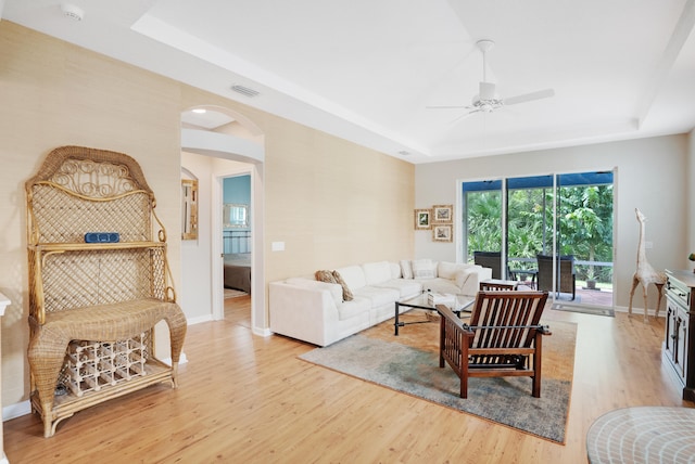 living room featuring light wood-type flooring, a tray ceiling, and ceiling fan