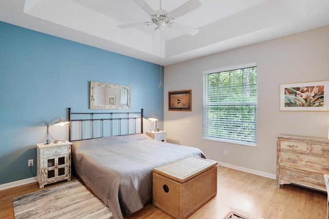 bedroom with ceiling fan, a raised ceiling, and light hardwood / wood-style flooring