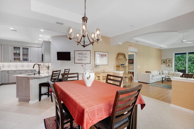 dining space featuring ceiling fan with notable chandelier, a tray ceiling, light hardwood / wood-style floors, and sink