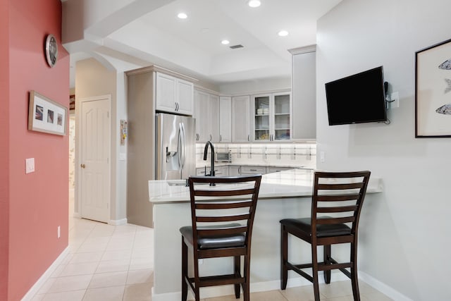 kitchen with light tile patterned floors, kitchen peninsula, tasteful backsplash, stainless steel fridge with ice dispenser, and a kitchen bar