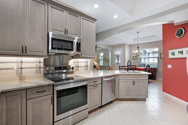 kitchen featuring appliances with stainless steel finishes, backsplash, a tray ceiling, sink, and a notable chandelier