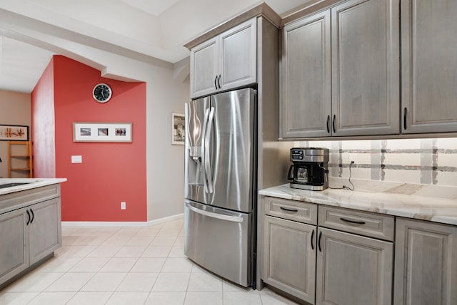 kitchen featuring stainless steel fridge, light stone countertops, light tile patterned floors, and tasteful backsplash