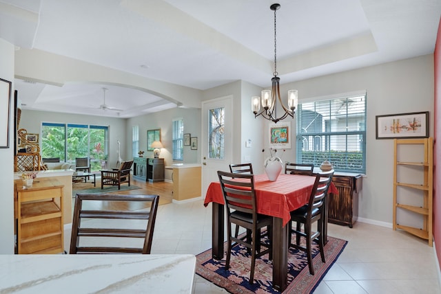 tiled dining space featuring ceiling fan with notable chandelier and a tray ceiling