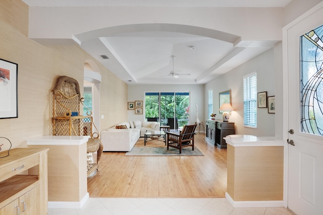 living room featuring ceiling fan, light hardwood / wood-style flooring, and a tray ceiling