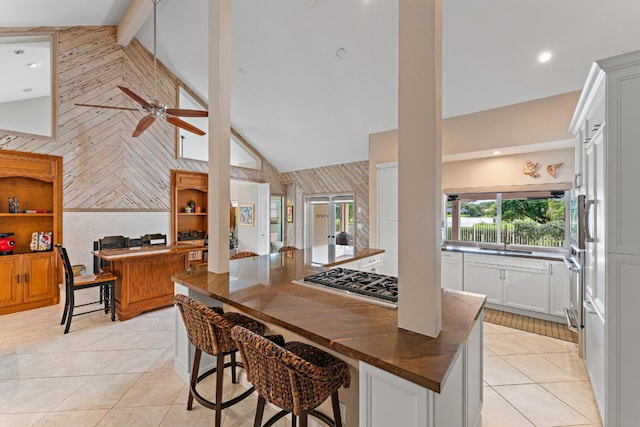 kitchen with high vaulted ceiling, white cabinets, beamed ceiling, a breakfast bar area, and stainless steel appliances