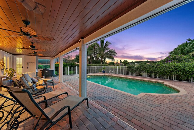 pool at dusk featuring an outdoor living space, ceiling fan, and a patio area