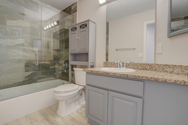 full bathroom featuring wood-type flooring, vanity, toilet, and bath / shower combo with glass door