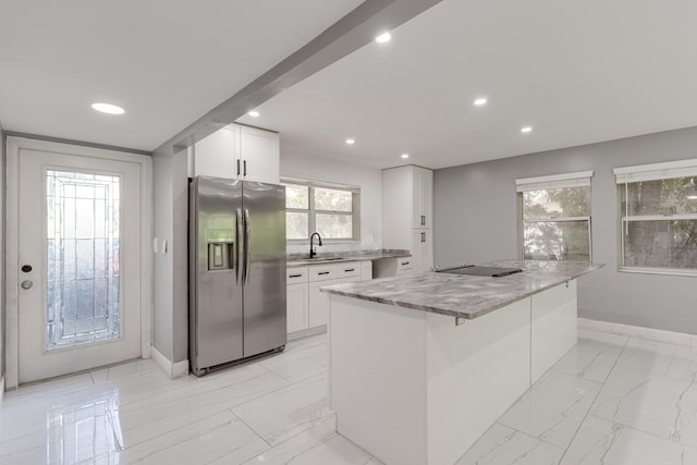 kitchen with light stone counters, sink, a kitchen island, white cabinetry, and stainless steel refrigerator with ice dispenser