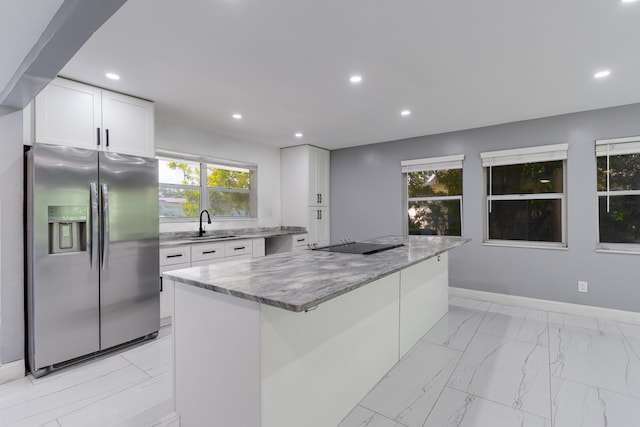 kitchen with a kitchen island, stainless steel fridge, white cabinetry, and light stone countertops