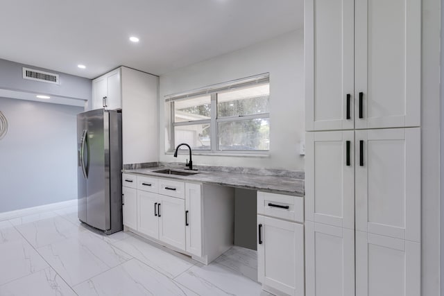 kitchen featuring light stone counters, stainless steel fridge, sink, and white cabinetry